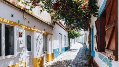 A Street With White Buildings And Flowers In Ferragudo